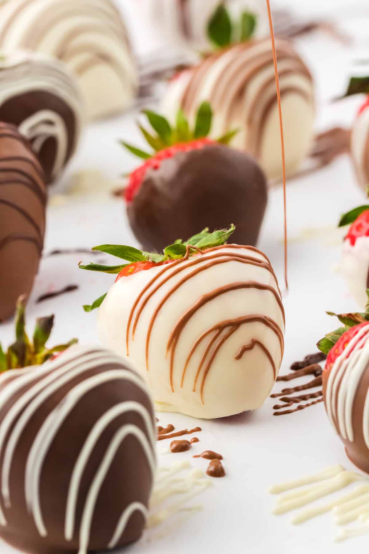 a white chocolate covered strawberry being drizzled with milk chocolate, surrounded by more chocolate covered strawberries