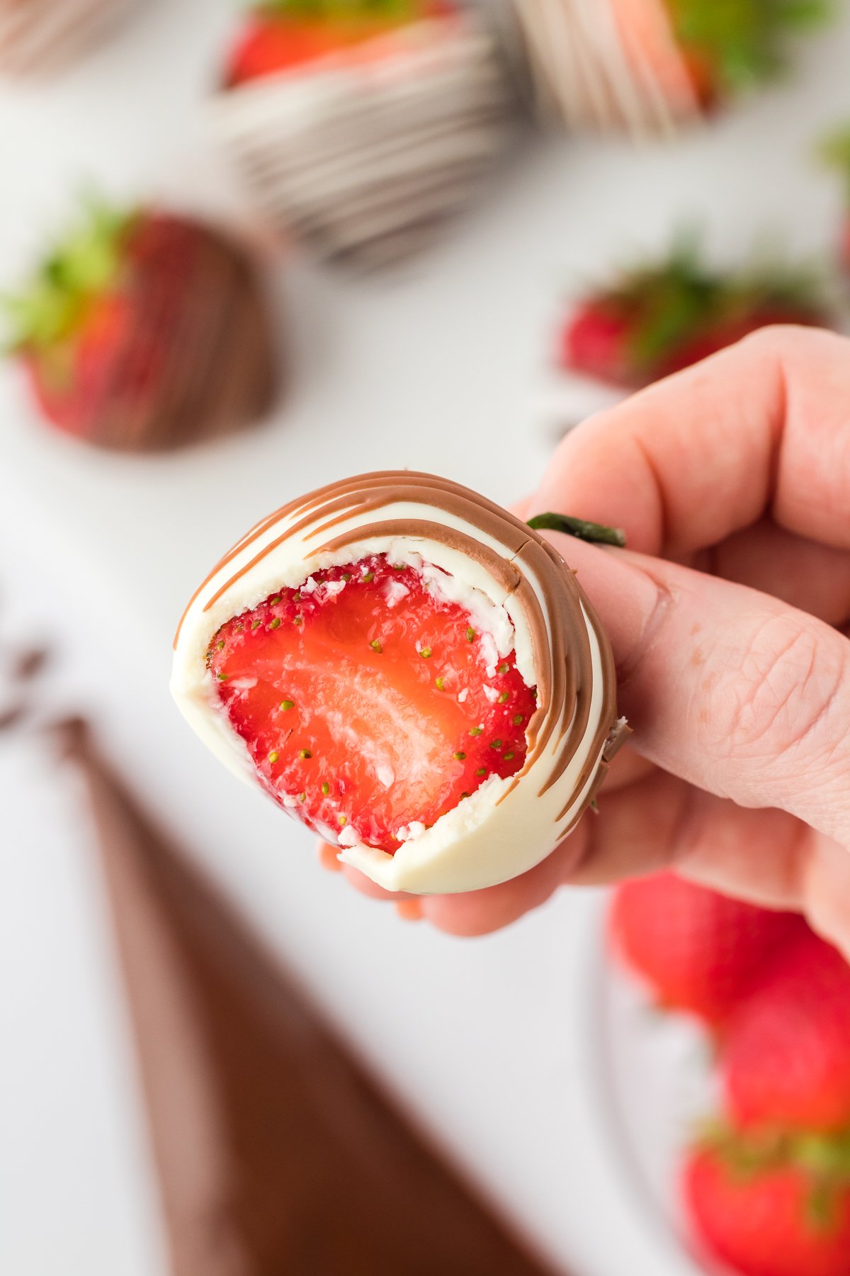 Close up of a hand holding a chocolate covered strawberry with one bite out of it, showing the fresh red strawberry inside