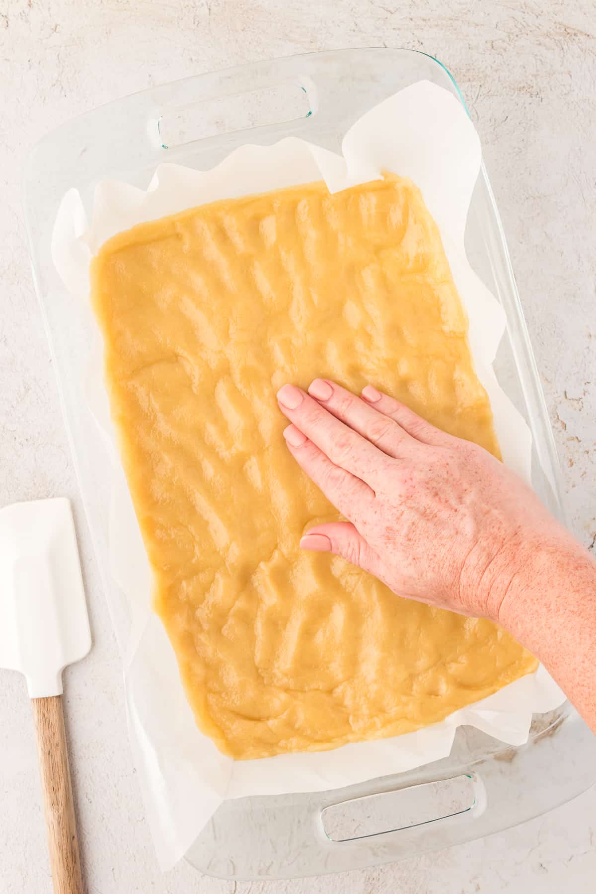 lemon bar dough flattened into a glass pan lined with parchment paper