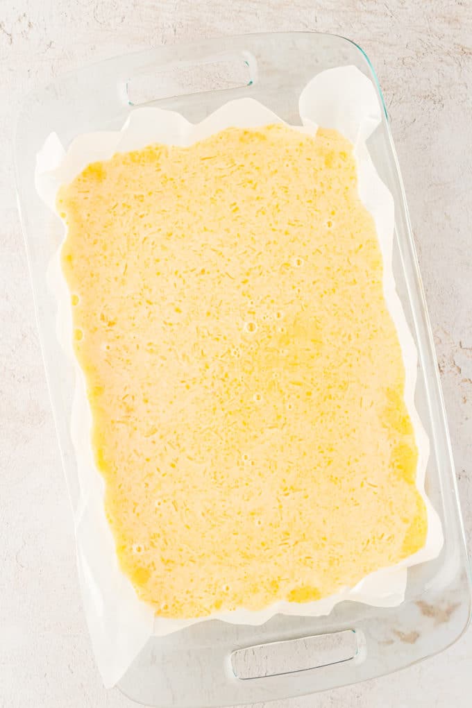 lemon bars in a glass pan lined with parchment paper before being baked