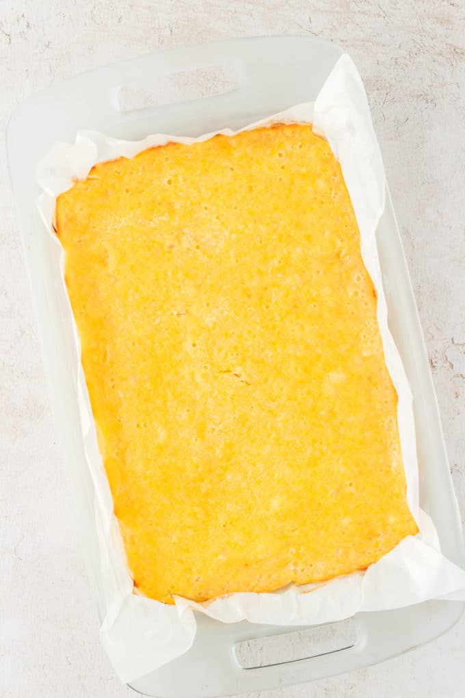 lemon bars in a glass pan lined with parchment paper that are cooked but have not been cut yet