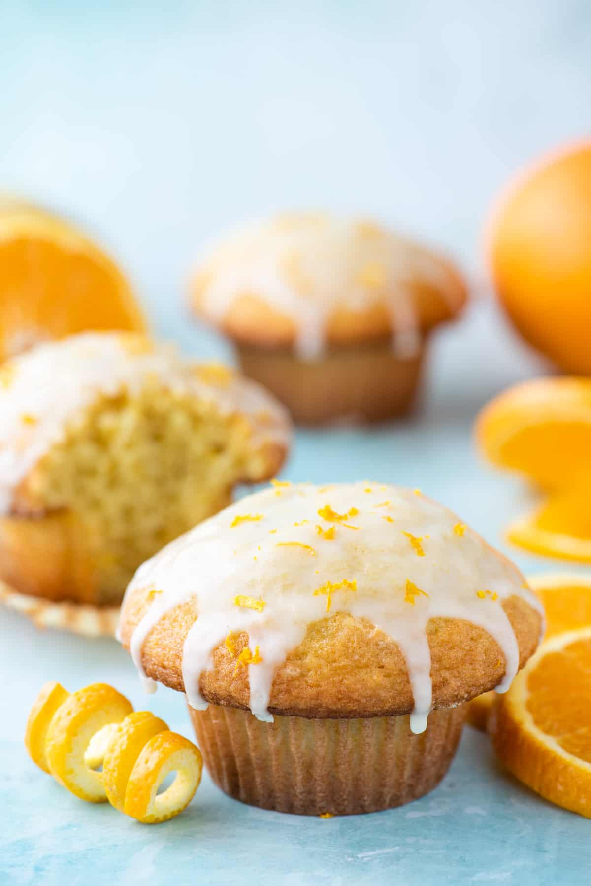 orange muffin surrounded by more muffins and orange slices on blue background 