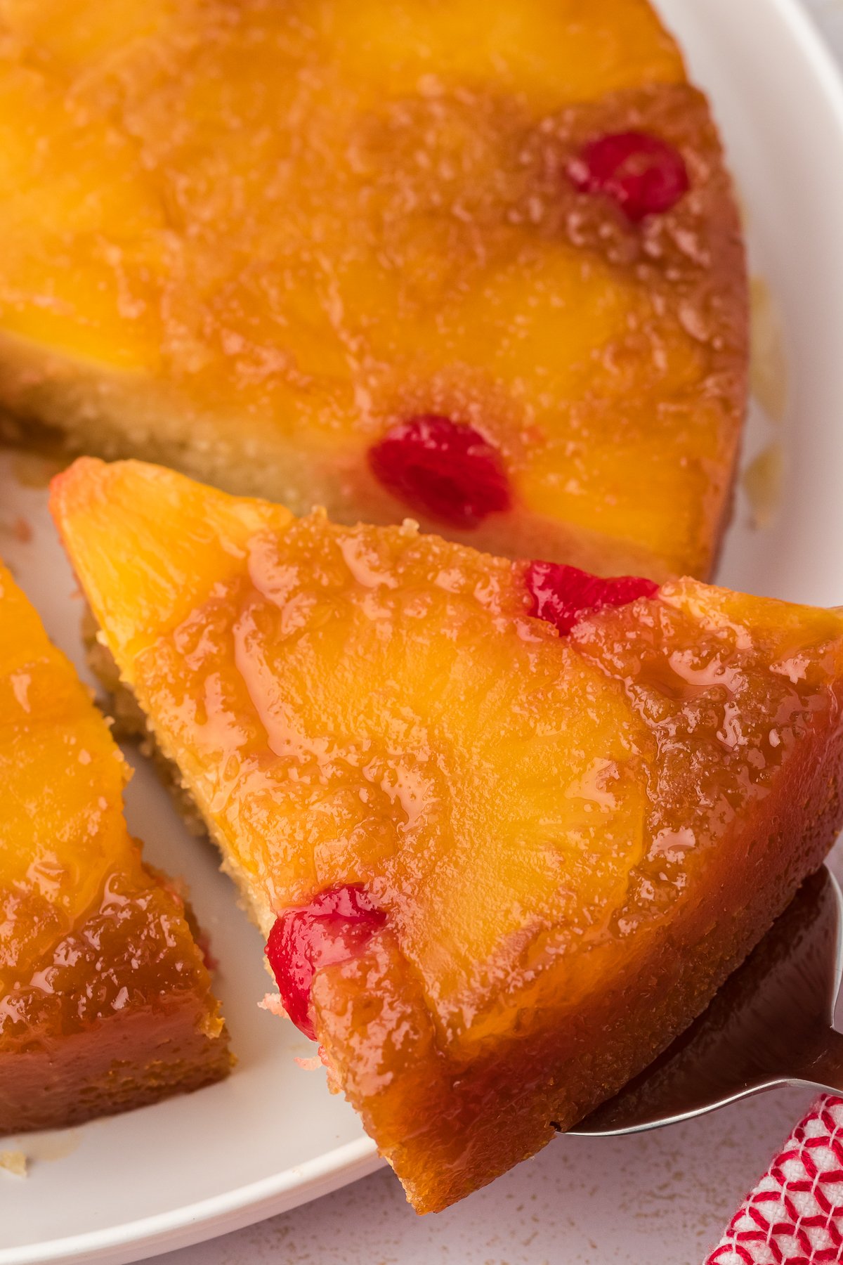 close up of a slice of pineapple upside down cake being lift off the plate away from the rest of the cake