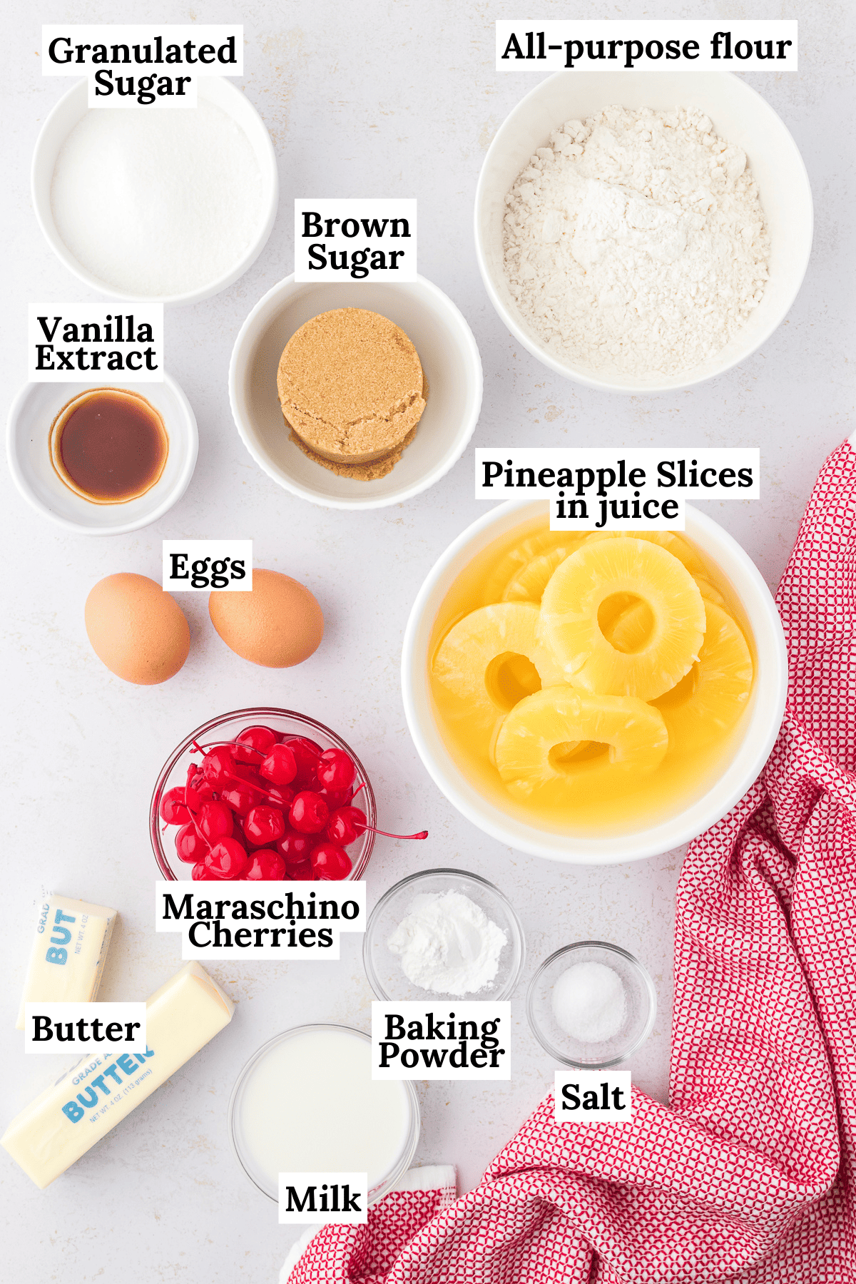 ingredients for pineapple upside down cake including granulated sugar, all-purpose flour, brown sugar, vanilla extract, brown sugar, eggs, pineapple slices, maraschino cherries, butter, baking powder, salt and milk