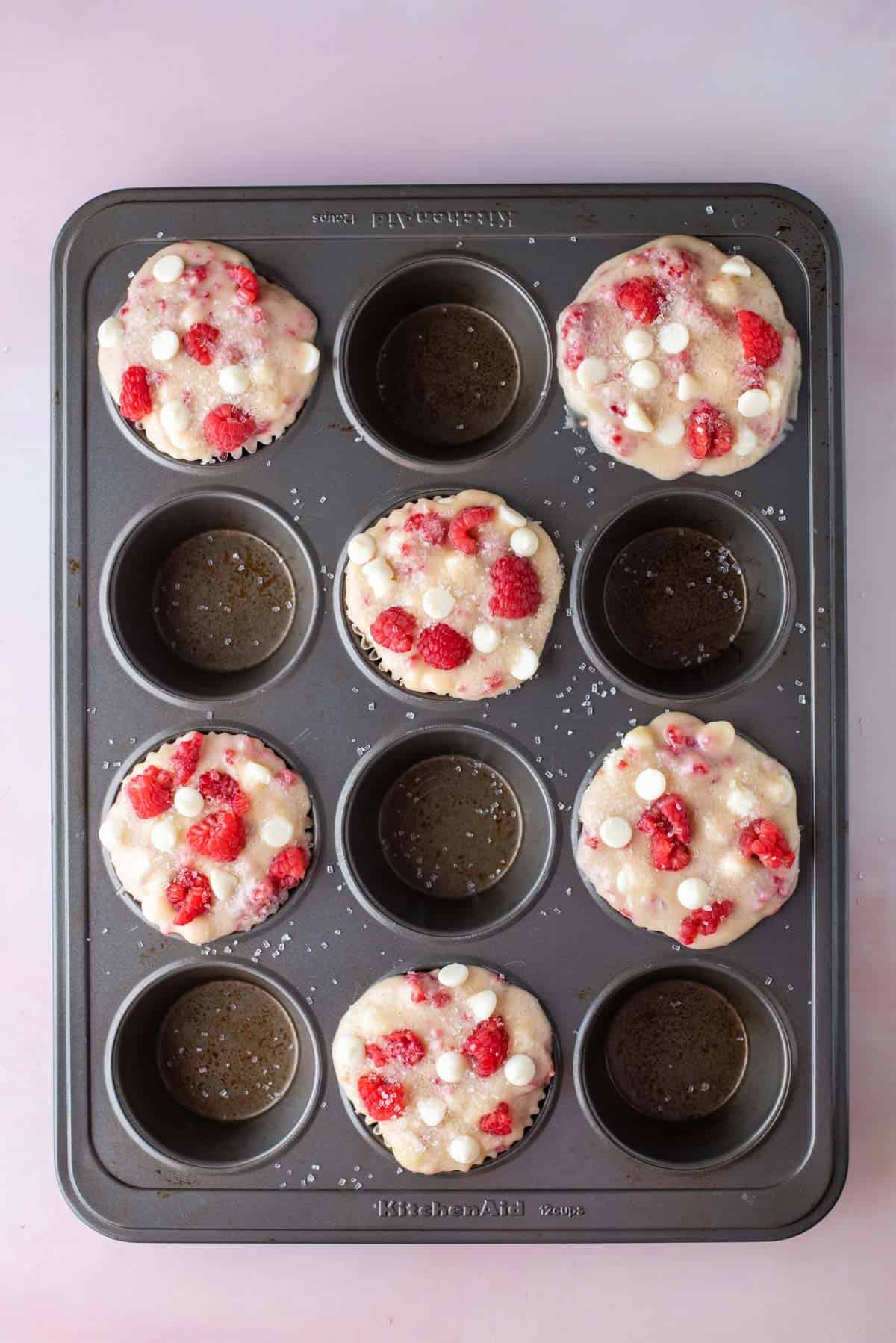 a muffin pan with raspberry white chocolate chip muffin batter filling every other muffin hole