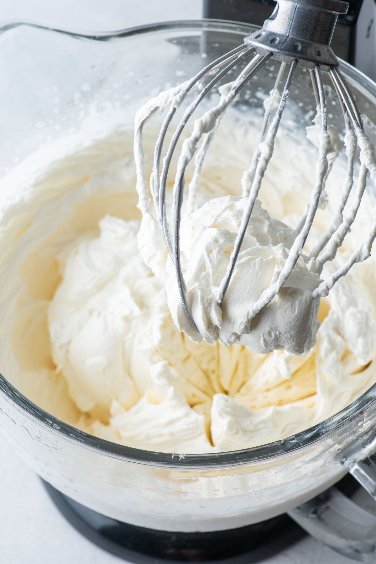 stabilized whipped cream mixed in an electric mixer with the mixer lifted and covered in whipped cream