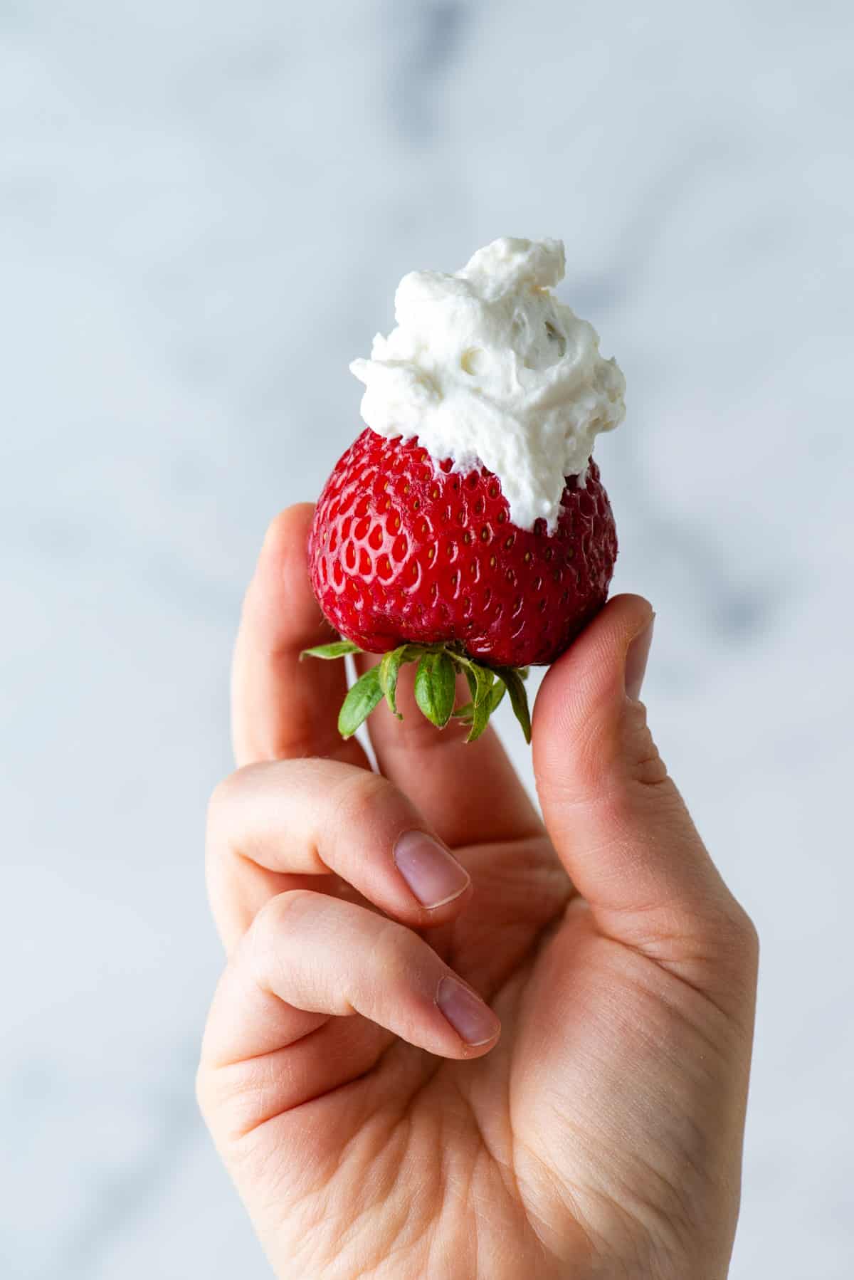 a hand holding a strawberry with stabilized whipped cream on top of it
