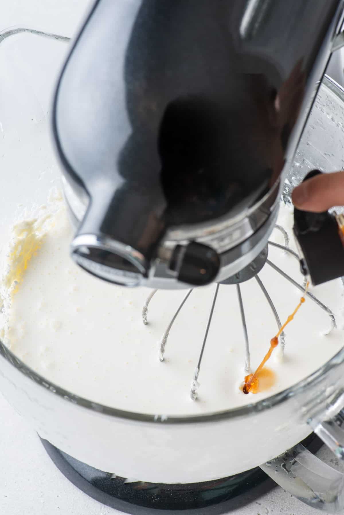 Vanilla extract being added to an electric mixer with other ingredients 