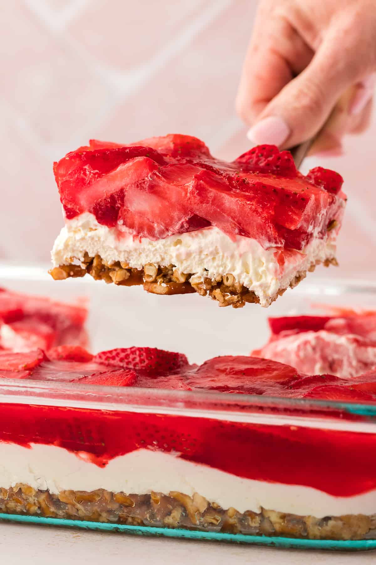 a slice of strawberry pretzel salad being lifted with a spatula out of a baking dish full of strawberry pretzel salad