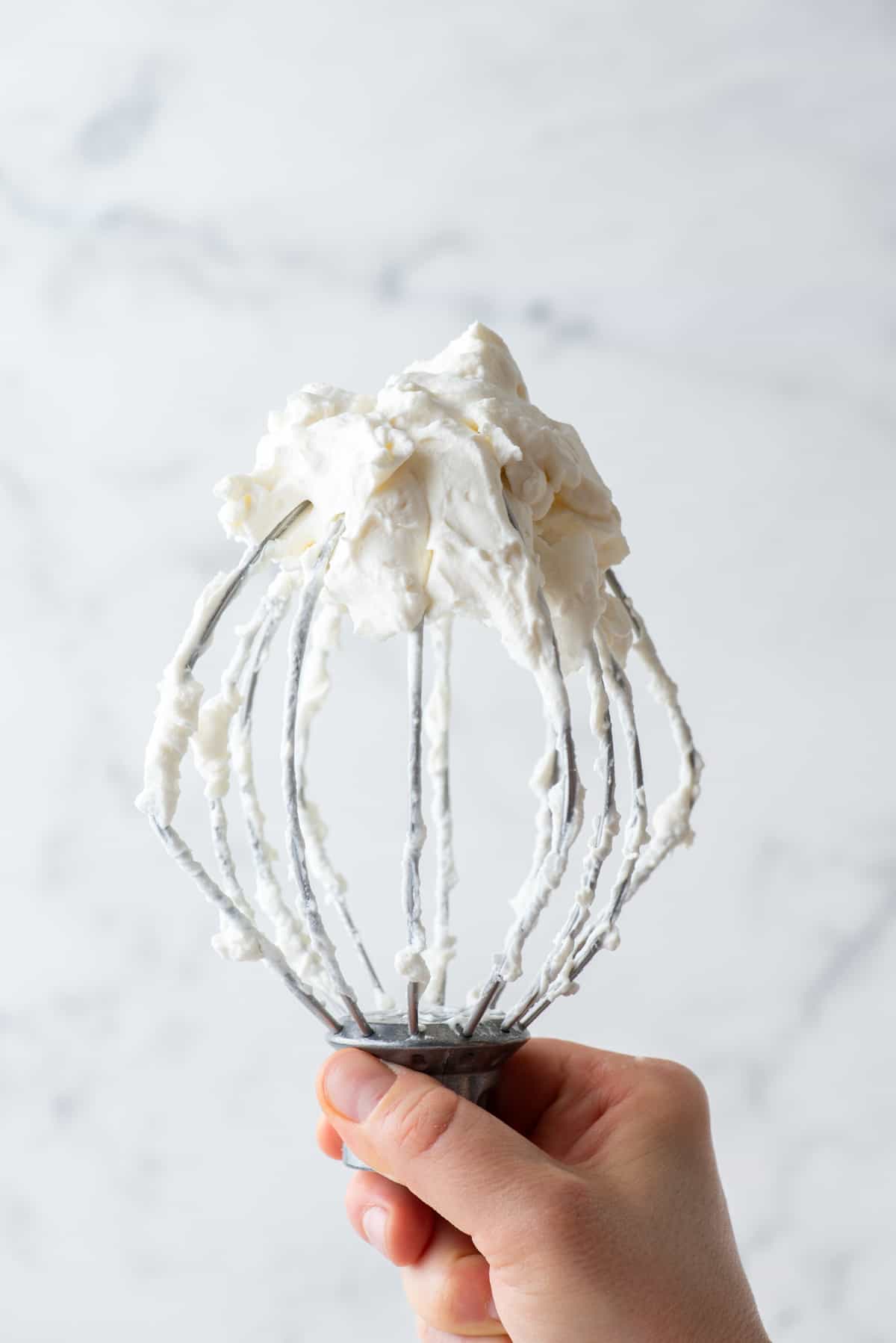 a hand holding up an electric mixer covered in fresh whipped cream