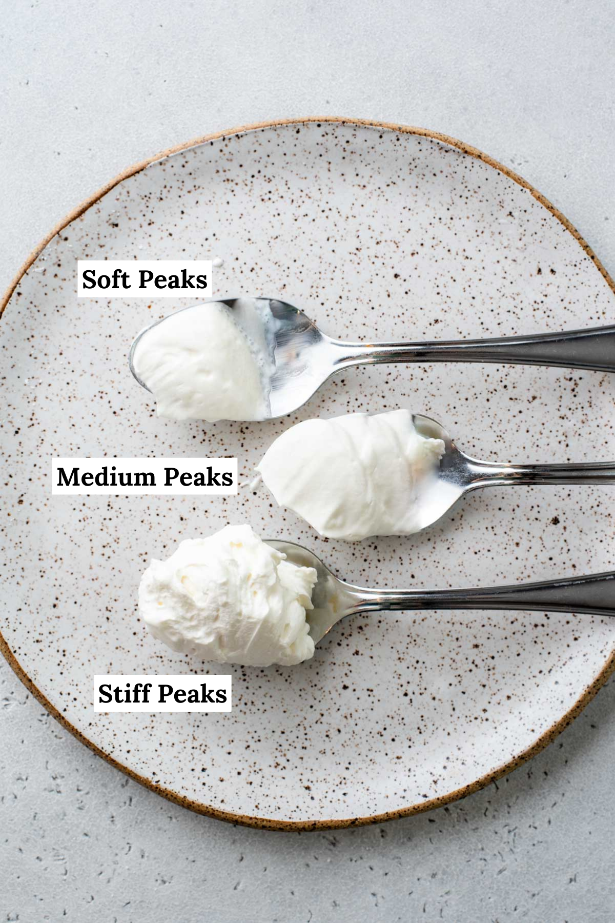 spoons of whipped cream on a plate with labels showing the different types of peaks: soft peaks, medium peaks, and stiff peaks