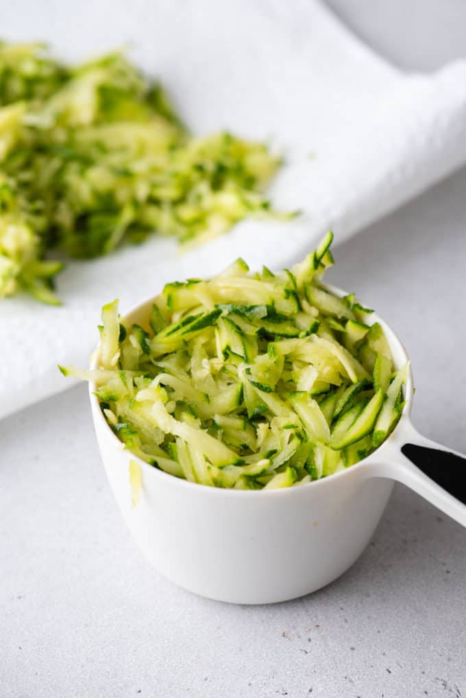shredded zucchini in a white measuring cup with more behind it on a paper towel