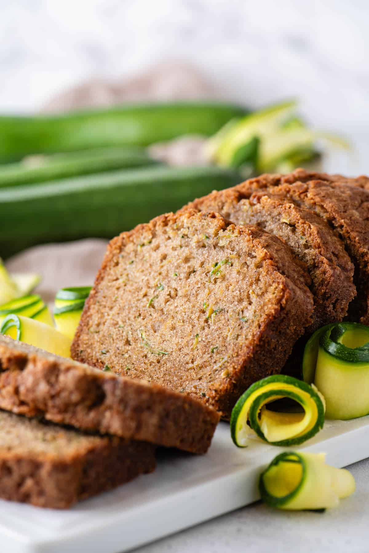 close up of a sliced loaf of zucchini bread with fresh zucchini slices around it and whole zucchinis in the background