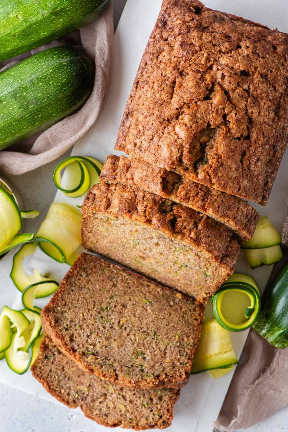 over top view of a loaf of zucchini bread that has been sliced, surrounded by fresh sliced zucchini and whole zucchini