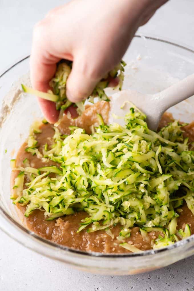 shredded zucchini being added to the top of a bowl full of bread batter