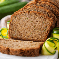 sliced zucchini bread on a white plate with fresh peels of zucchini surrounding it