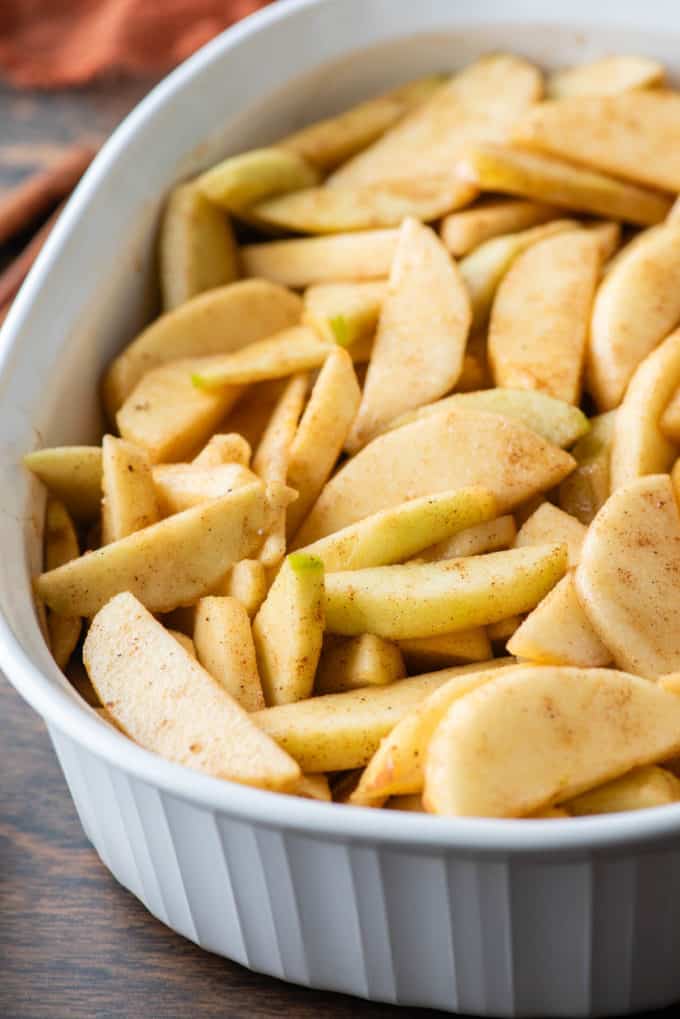 sliced apples in a white baking dish coated in a cinnamon mixture