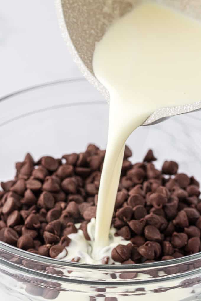 heavy cream being poured into a glass bowl full of semi-sweet chocolate chips