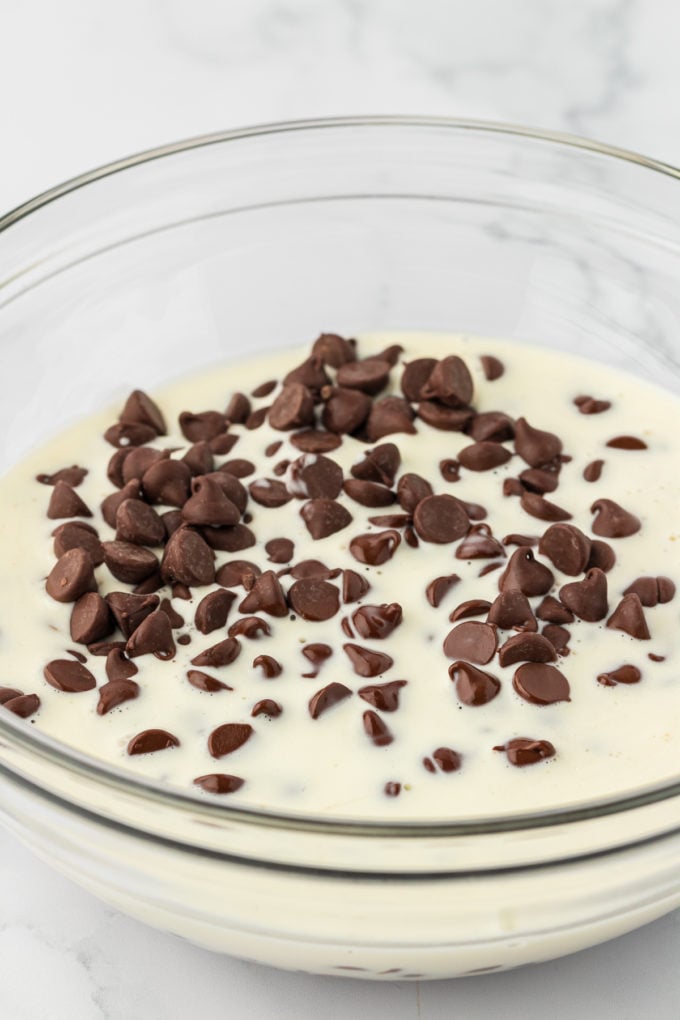 a clear glass bowl with heavy cream and semi-sweet chocolate chips in it