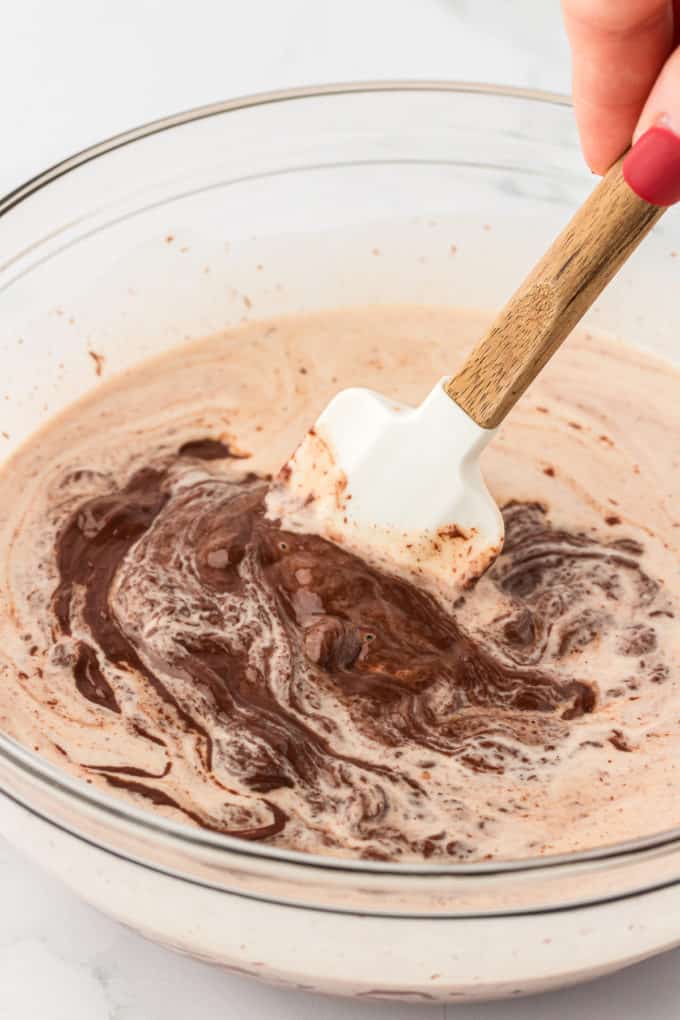 a clear glass bowl with chocolate and heavy cream being stirred in it with a white spatula