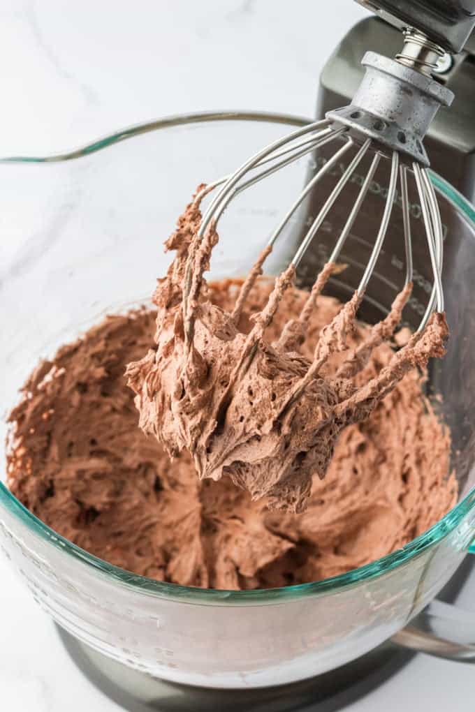 whipped ganache in an electric mixer with the mixer lifted and covered in ganache