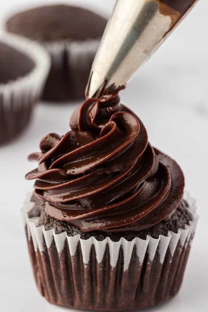 a chocolate cupcake with piped ganache being piped on top with a piping tip