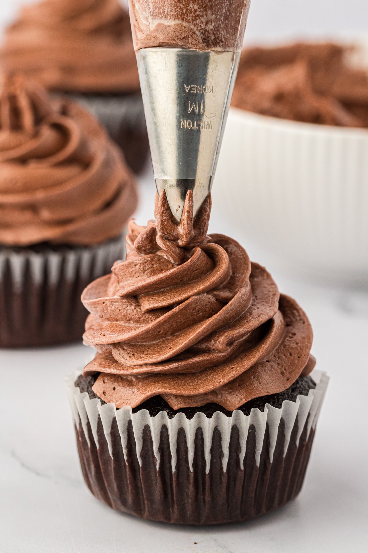 a chocolate cupcake with a whipped ganache being piped on top with a piping tip