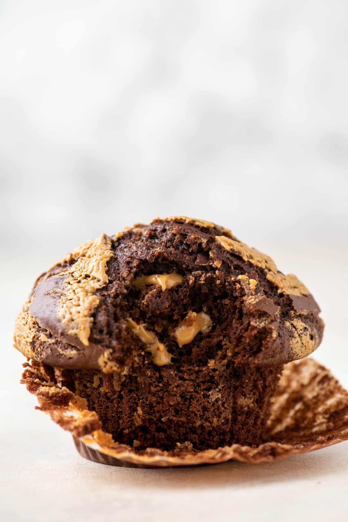 one chocolate peanut butter muffin with the muffin liner peeled partially off and a bite taken out