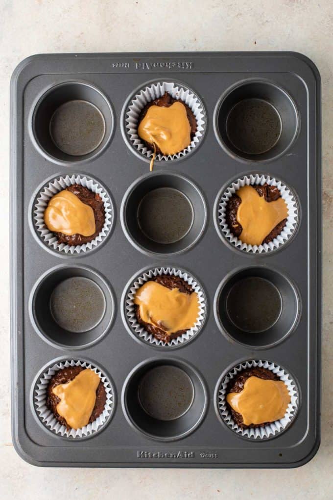 chocolate muffin batter with melted peanut butter on top of it in muffin liners in every other whole of a muffin pan