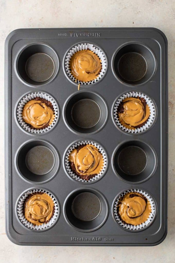 chocolate muffin batter with melted peanut butter on top of it in muffin liners in every other whole of a muffin pan