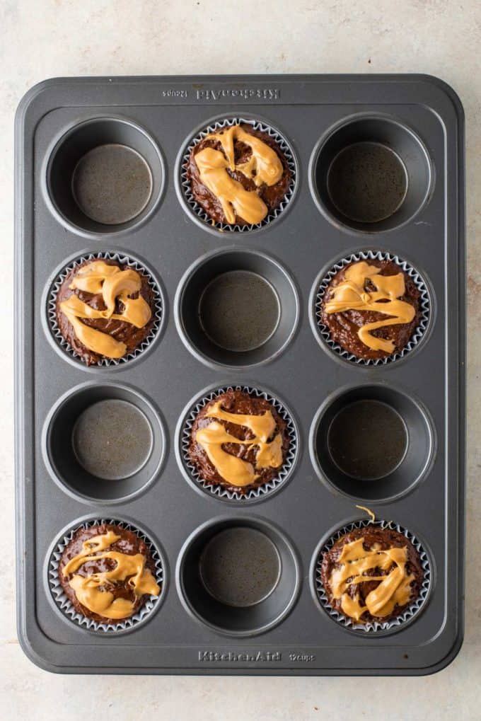 chocolate muffin batter with peanut butter on top in muffin liners in every other whole of a muffin pan