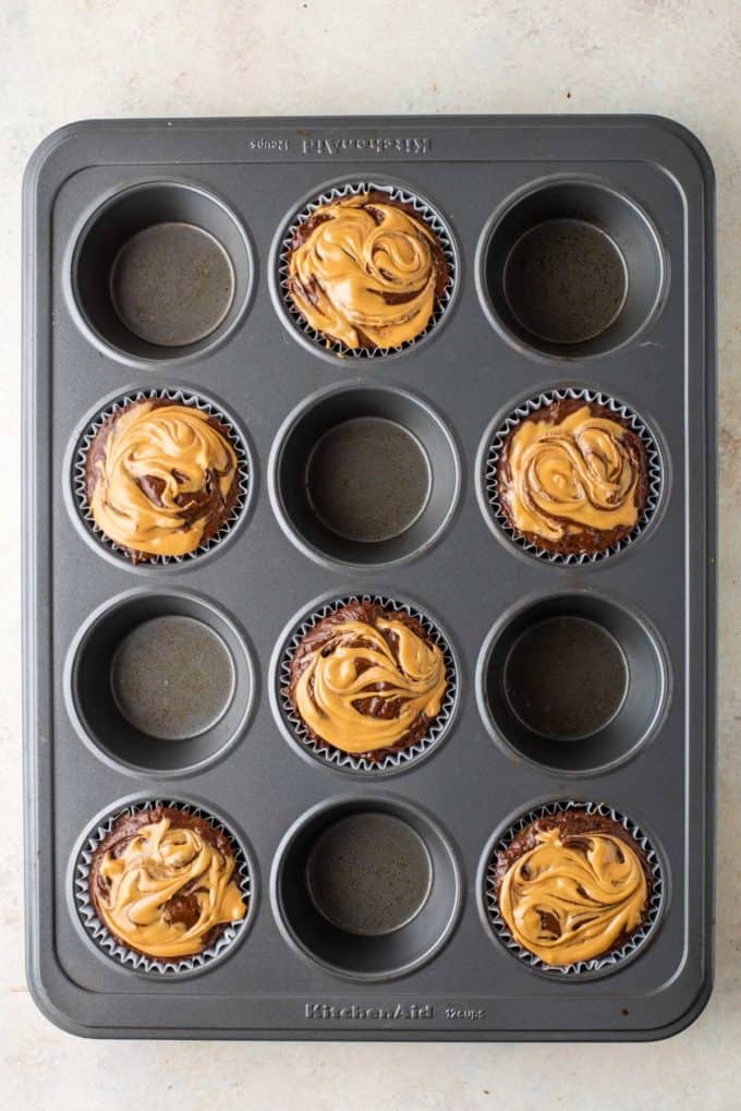 chocolate muffin batter with peanut butter on top in muffin liners in every other whole of a muffin pan
