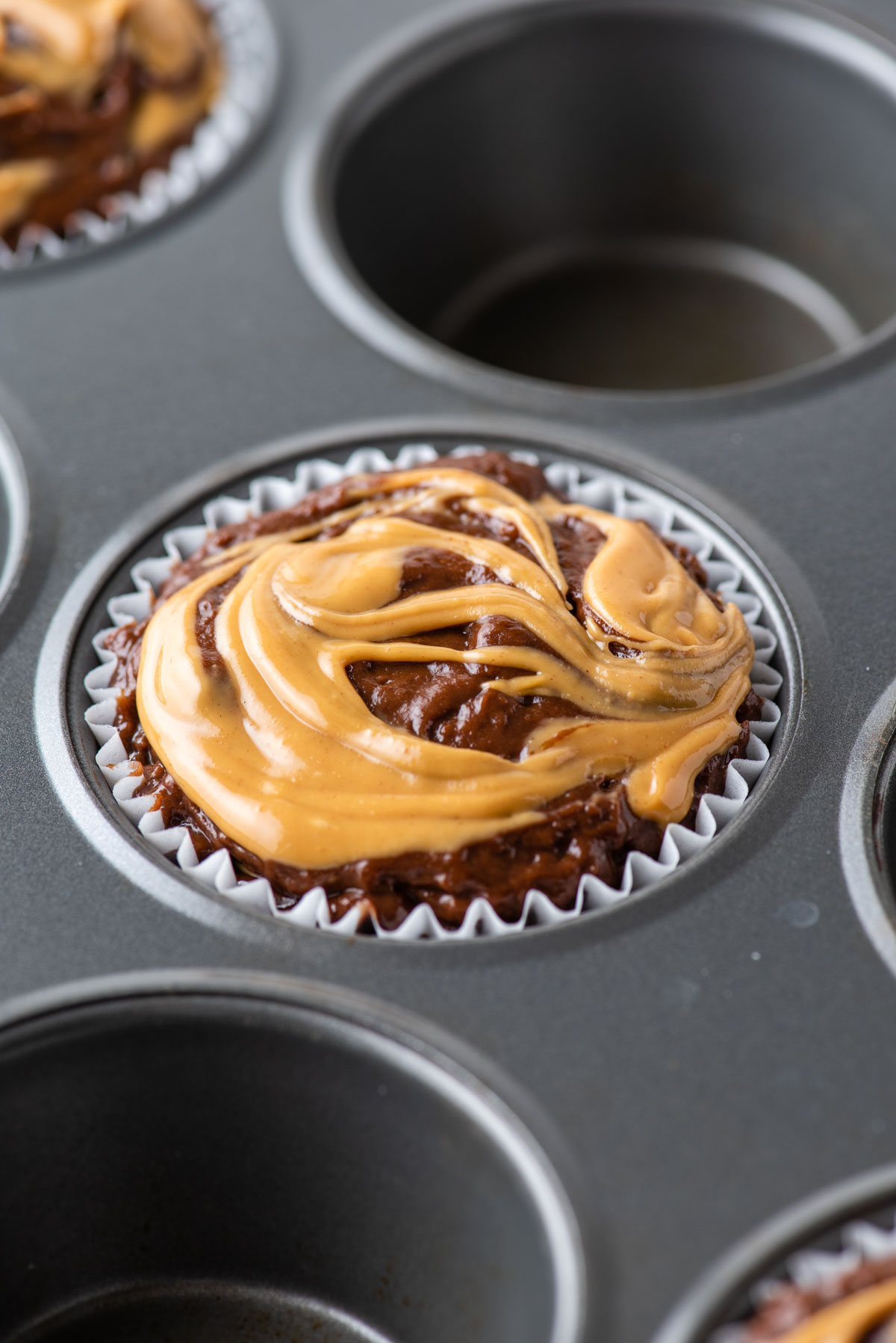 chocolate peanut butter muffin batter with peanut butter on top in a muffin tin