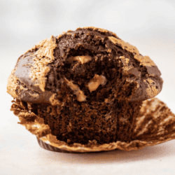one chocolate peanut butter muffin with the muffin liner peeled partially off and a bite taken out