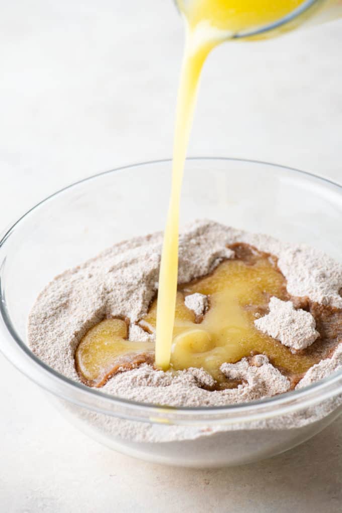 flour, brown sugar, cinnamon and salt in a clear glass bowl with melted butter being poured in