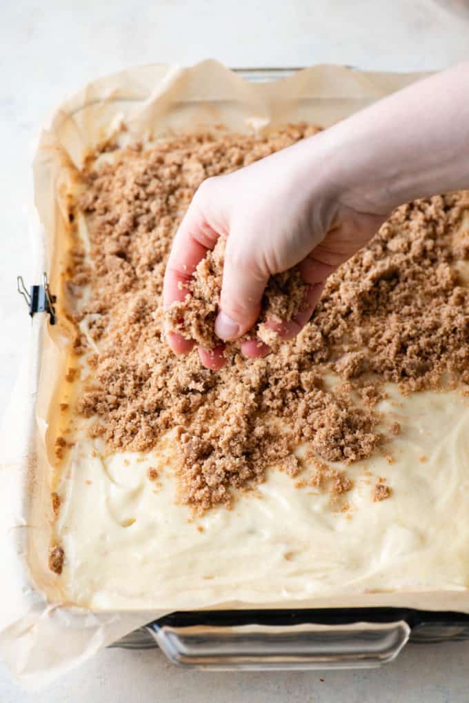 crumb topping being sprinkled over coffee cake batter in a baking pan lined with parchment paper