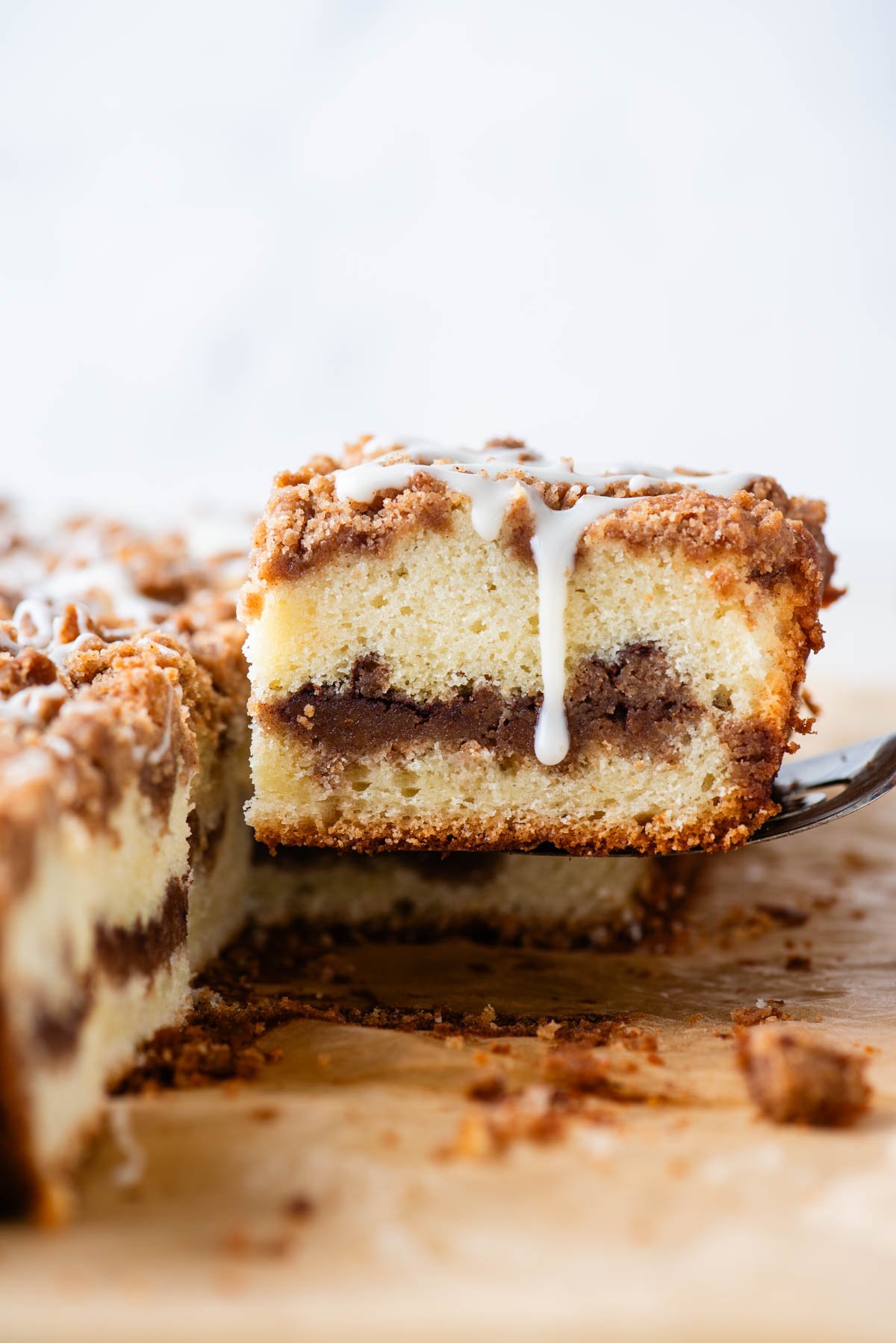a slice of coffee cake with glaze dripping down the side of it being lifted by a spatula away from the rest of the coffee cake