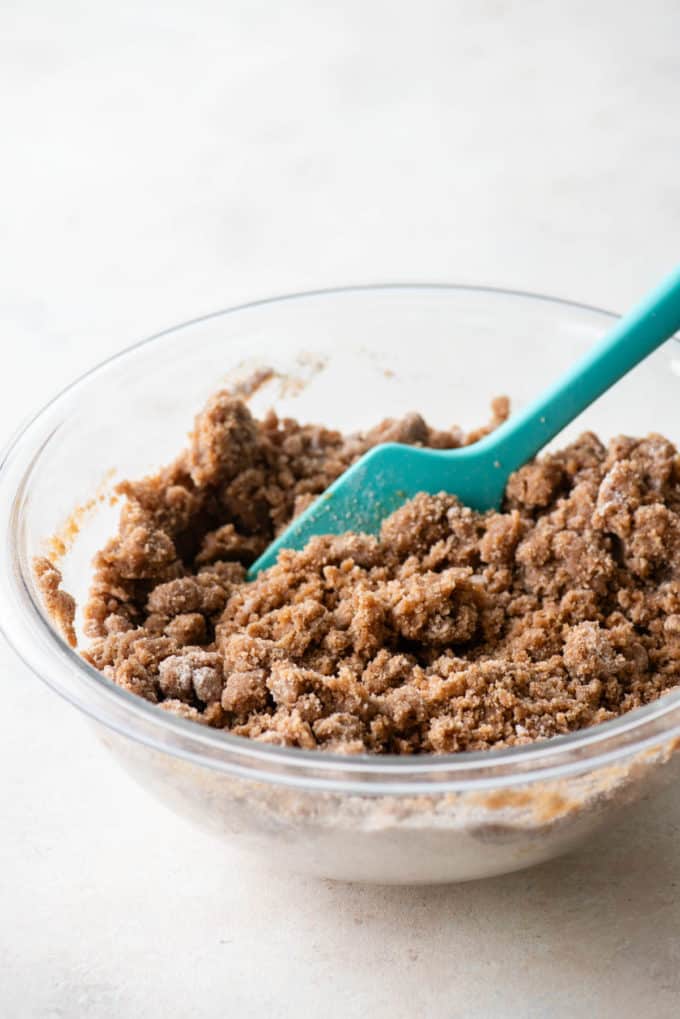 crumb topping for coffee cake in a clear glass bowl with a teal spatula in it