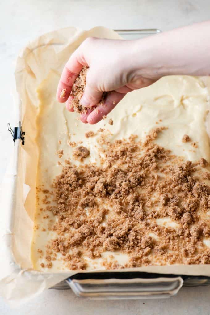 crumb topping being sprinkled in a baking pan lined with parchment paper