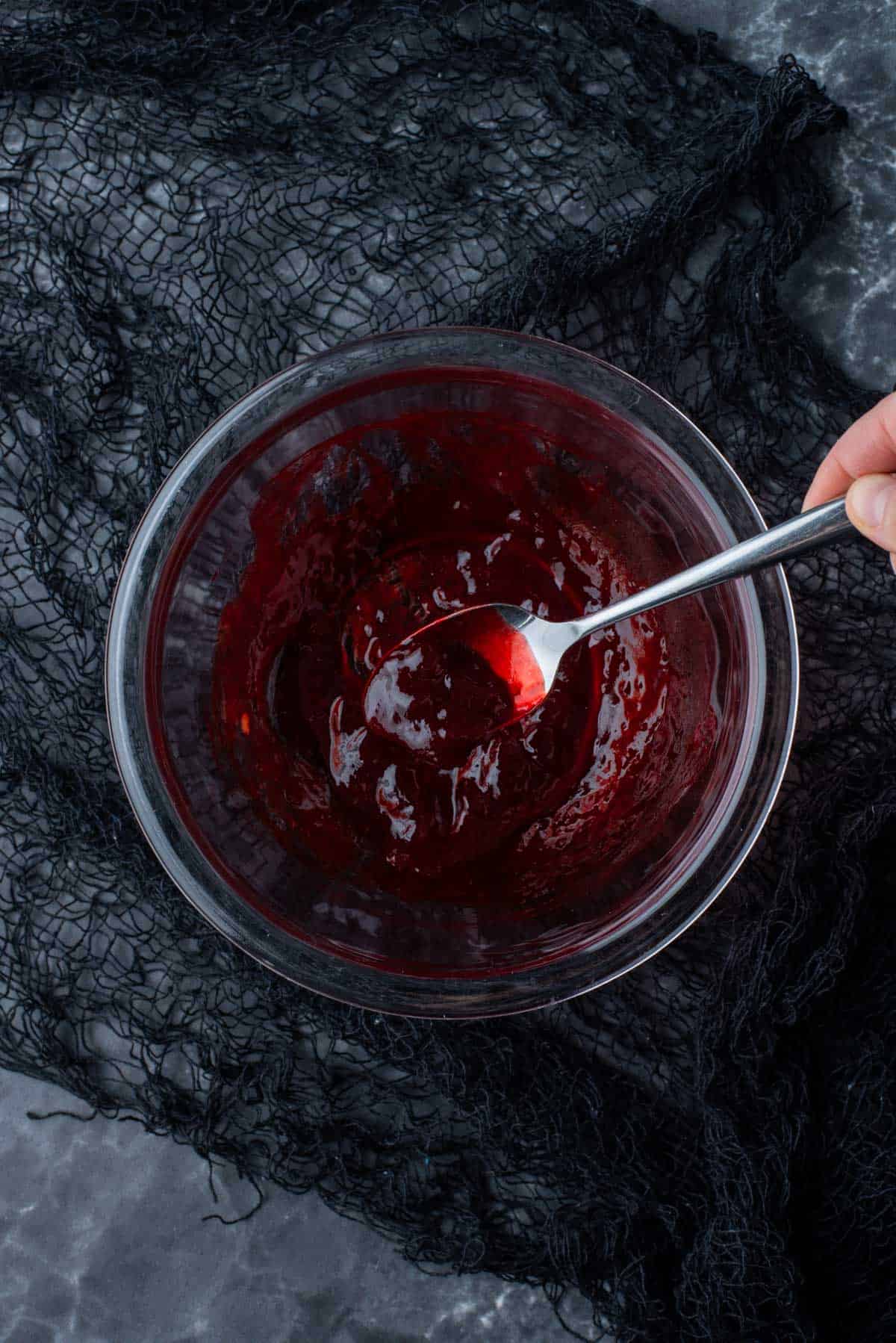 blood jam being mixed in a clear glass bowl on a black surface for eyeball cupcakes