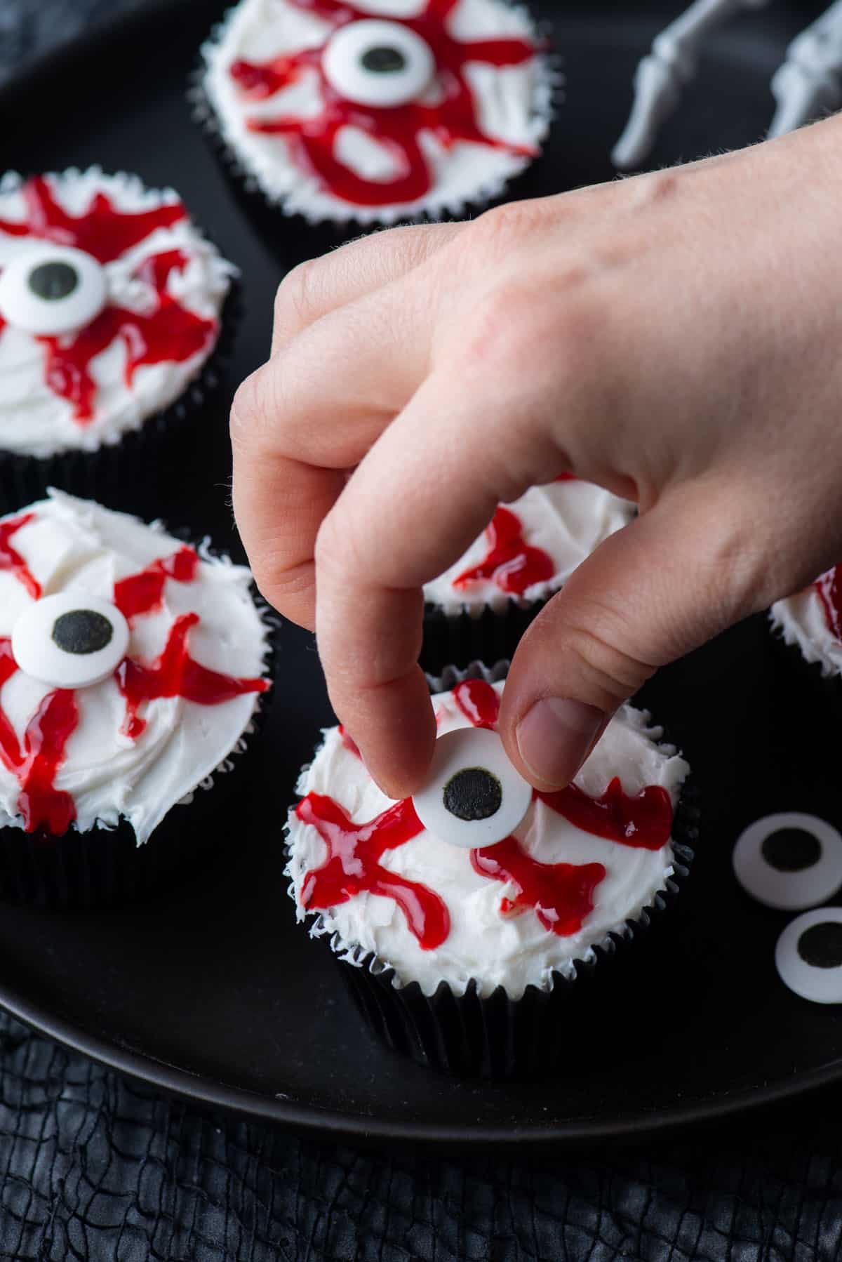 placing a candy eyeball on an eyeball cupcake with more eyeball cupcakes completed around it
