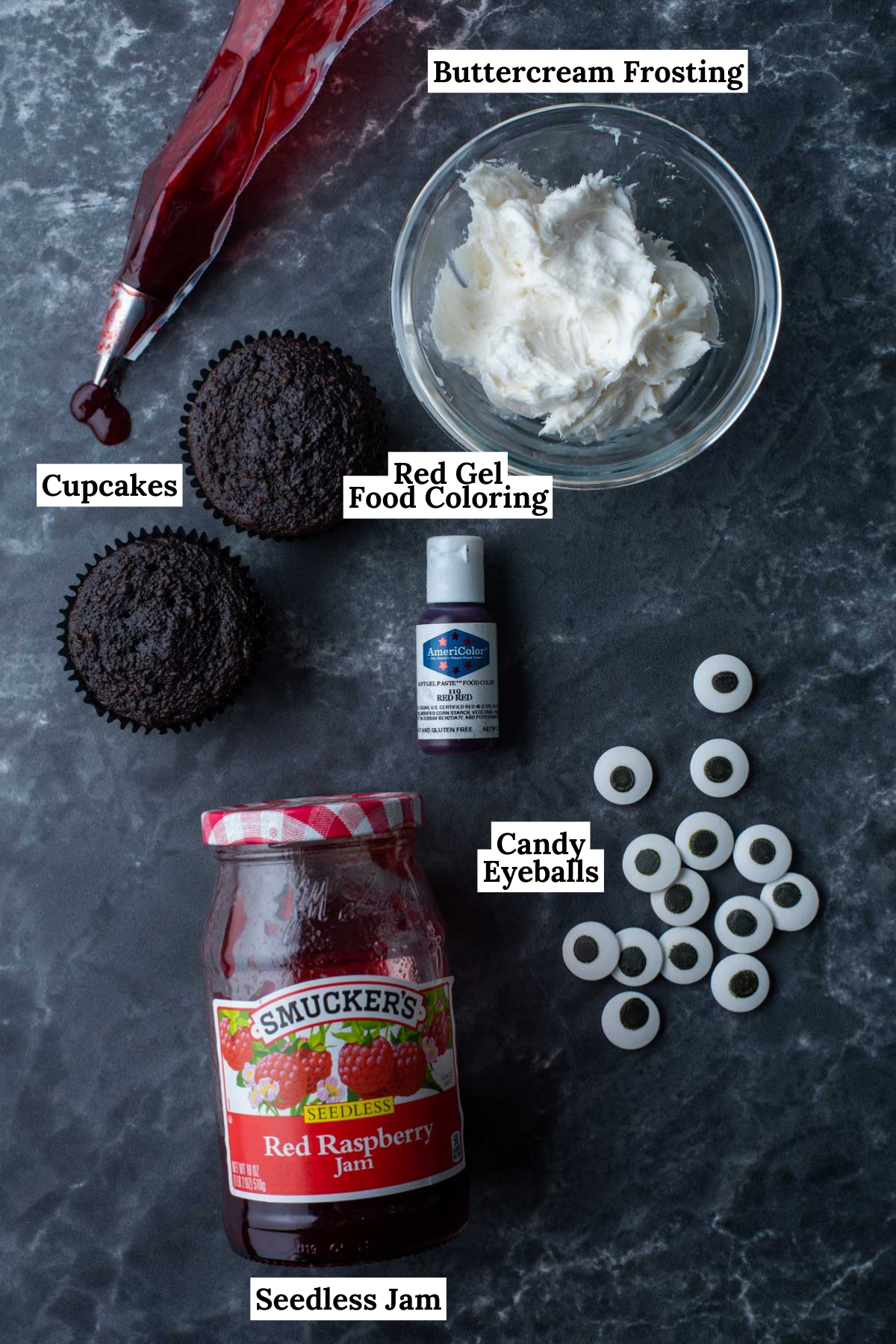 ingredients for eyeball cupcakes including chocolate cupcakes, red gel food coloring, candy eyebals, white frosting and jam