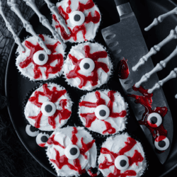eyeball cupcakes on a black plate with a large knife and skeleton hands