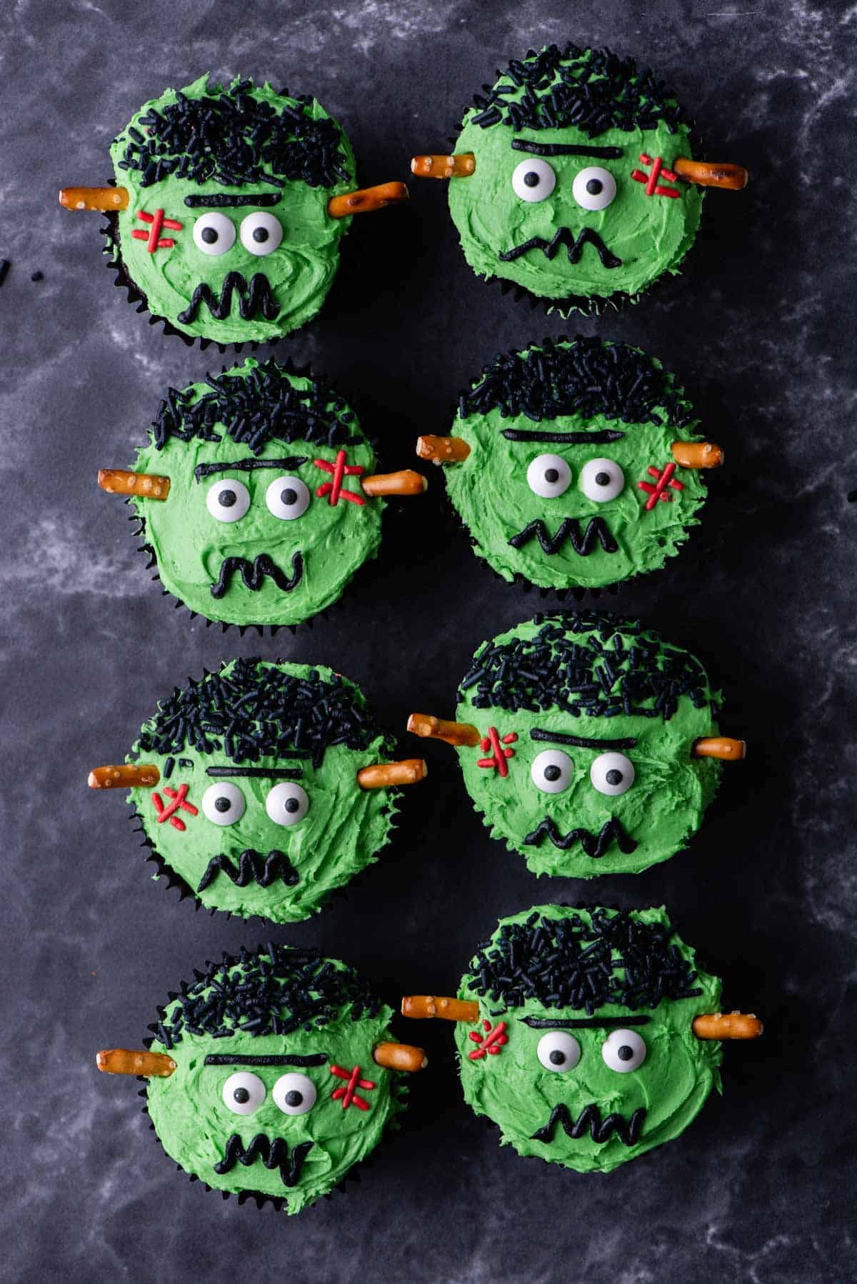 frankenstein cupcakes arranged in two rows on a grey surface