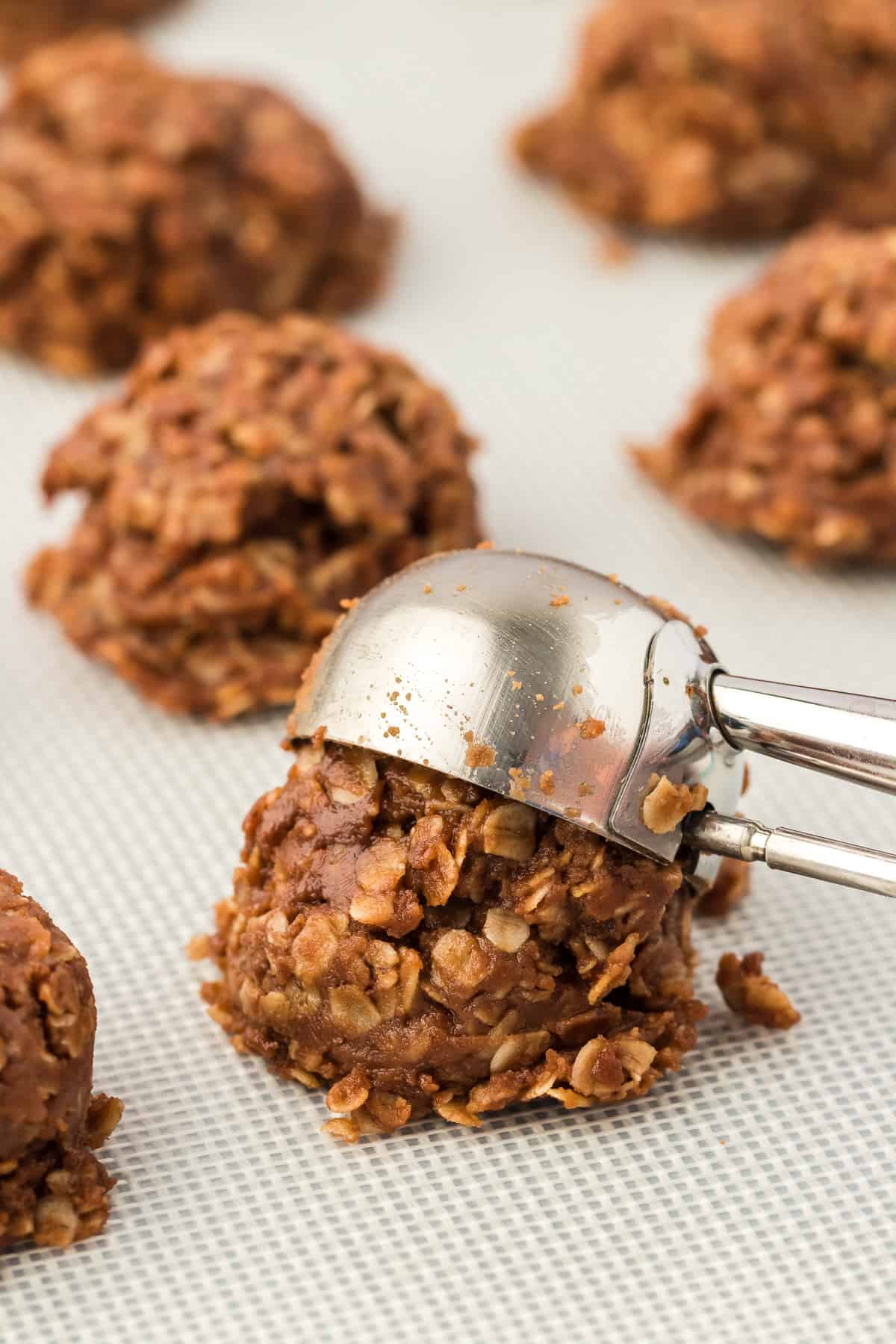 no bake cookies being dropped onto a lined baking sheet with a cookie scoop
