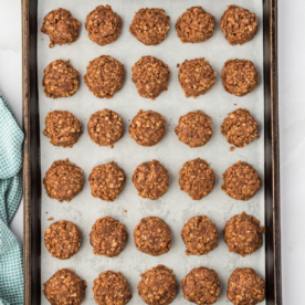 no bake cookies lined up filling up a baking sheet lined with parchment paper with a blue kitchen towel to the left of it