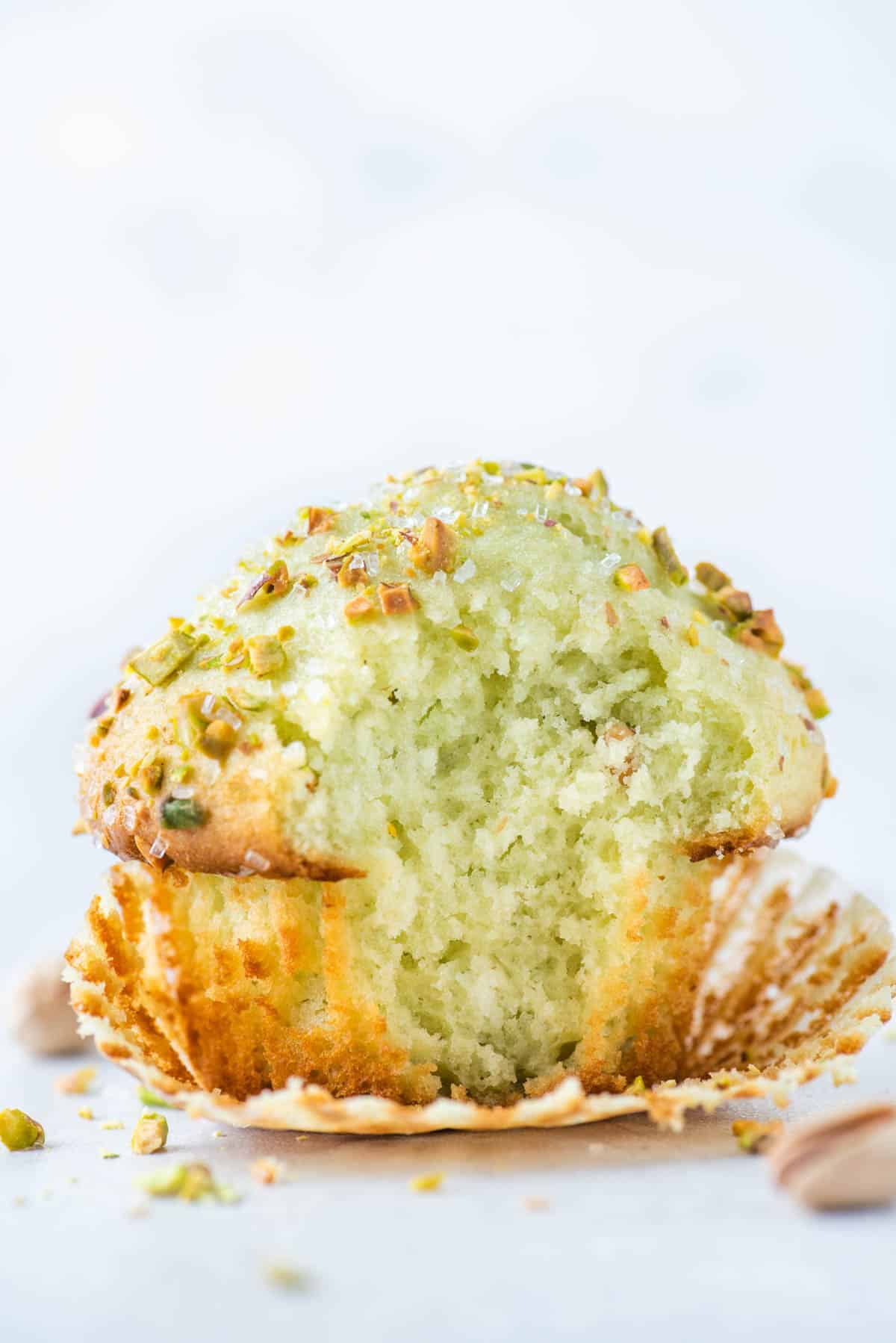 a pistachio muffin with the muffin paper partially pulled off and a bite taken out