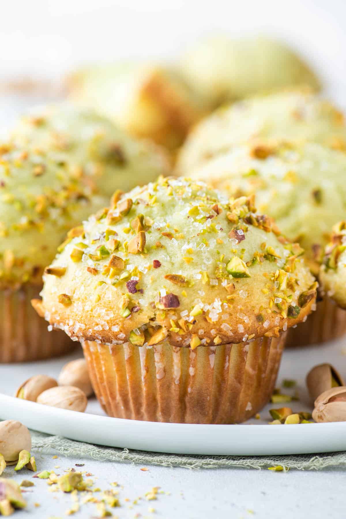pistachio muffins on a white plate with whole pistachios sprinkled around