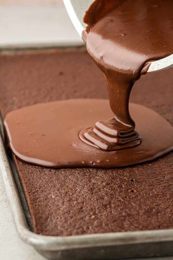 chocolate frosting being poured over a chocolate texas sheet cake