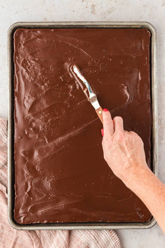 chocolate frosting being spread onto a chocolate texas sheet cake with a butter knife 